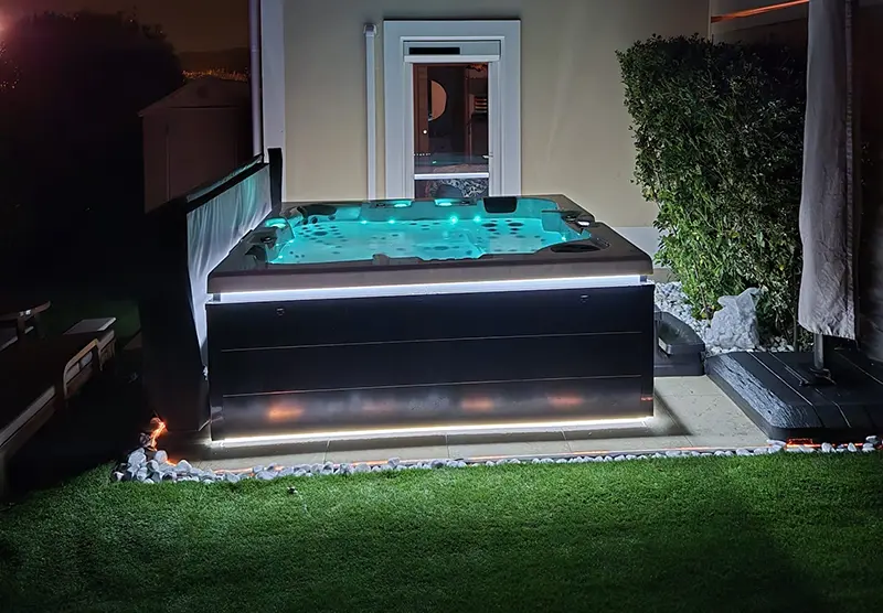 Un spa thérapeutique 5 personnes éclairé dans la nuit, devant une maison moderne à Fréjus