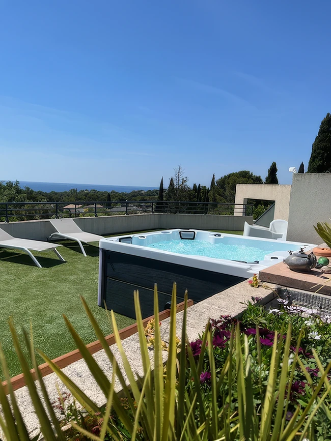 Le spa Amalfi est installé sur un toit-terrasse à Saint-Raphaël, avec de l'eau bouillonnante. Deux chaises longues sont posées sur le gazon synthétique, avec une vue sur la mer Méditerranée à l'horizon.