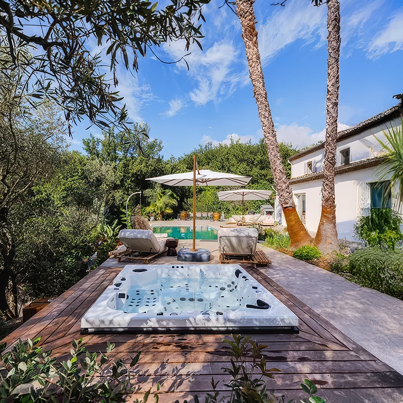 Spa haut de gamme thérapeutique 5 places modèle Napoli Luxe encastré dans la terrasse en bois d'une villa avec piscine et palmiers à Tourrette-sur-Loup.